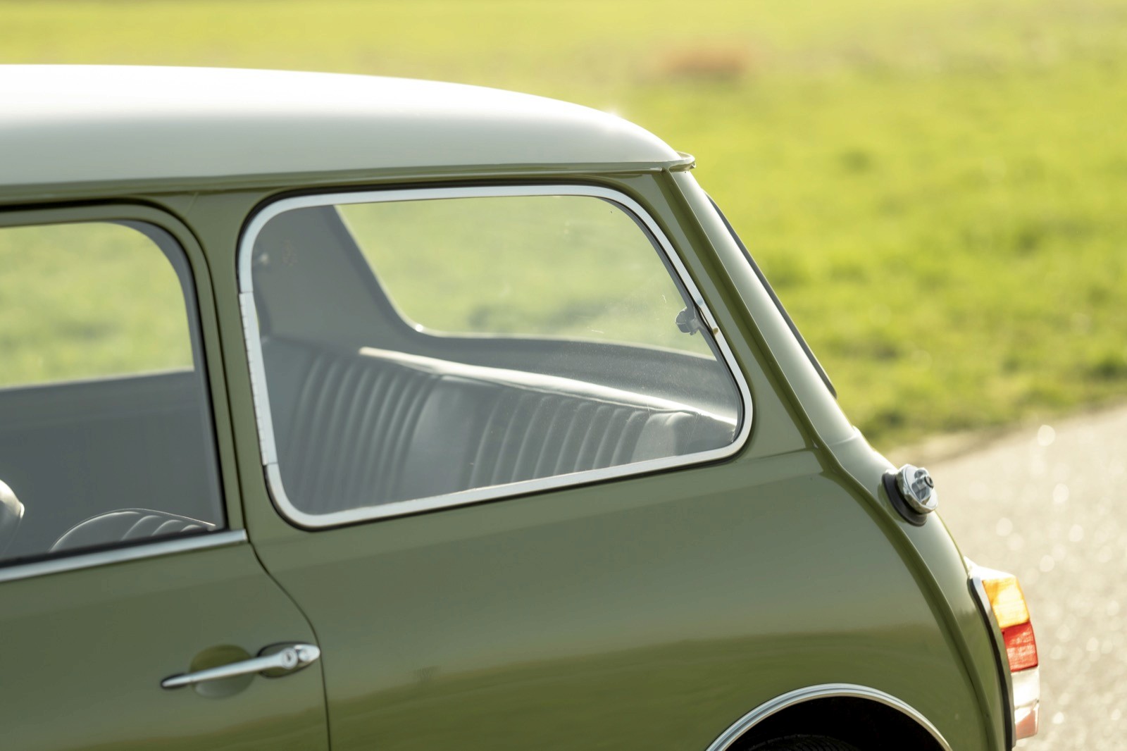 Close-up of a green vintage car's side window, with grassy landscape blurred in the background.
