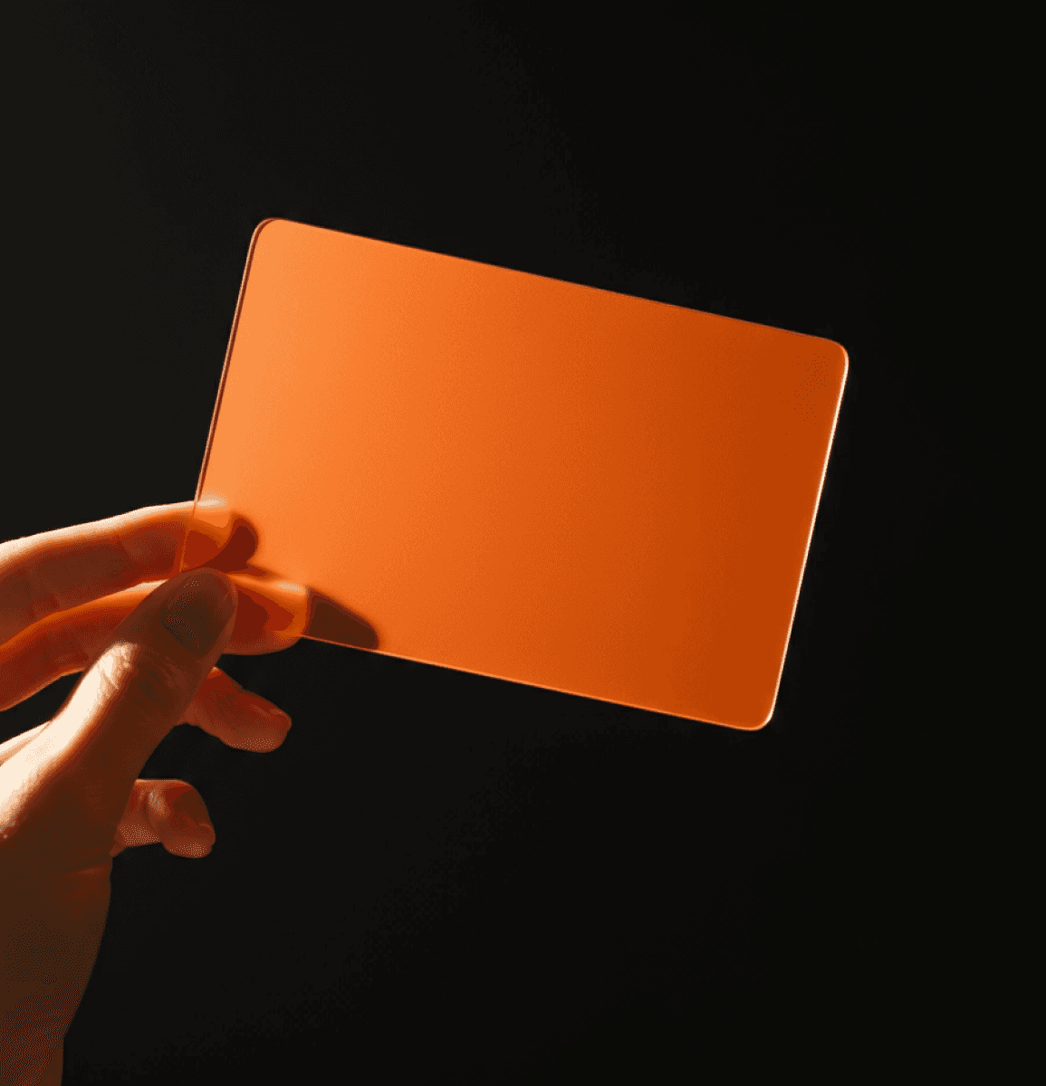 A close-up of a hand holding a vibrant orange card against a dark background, illuminated by warm light.