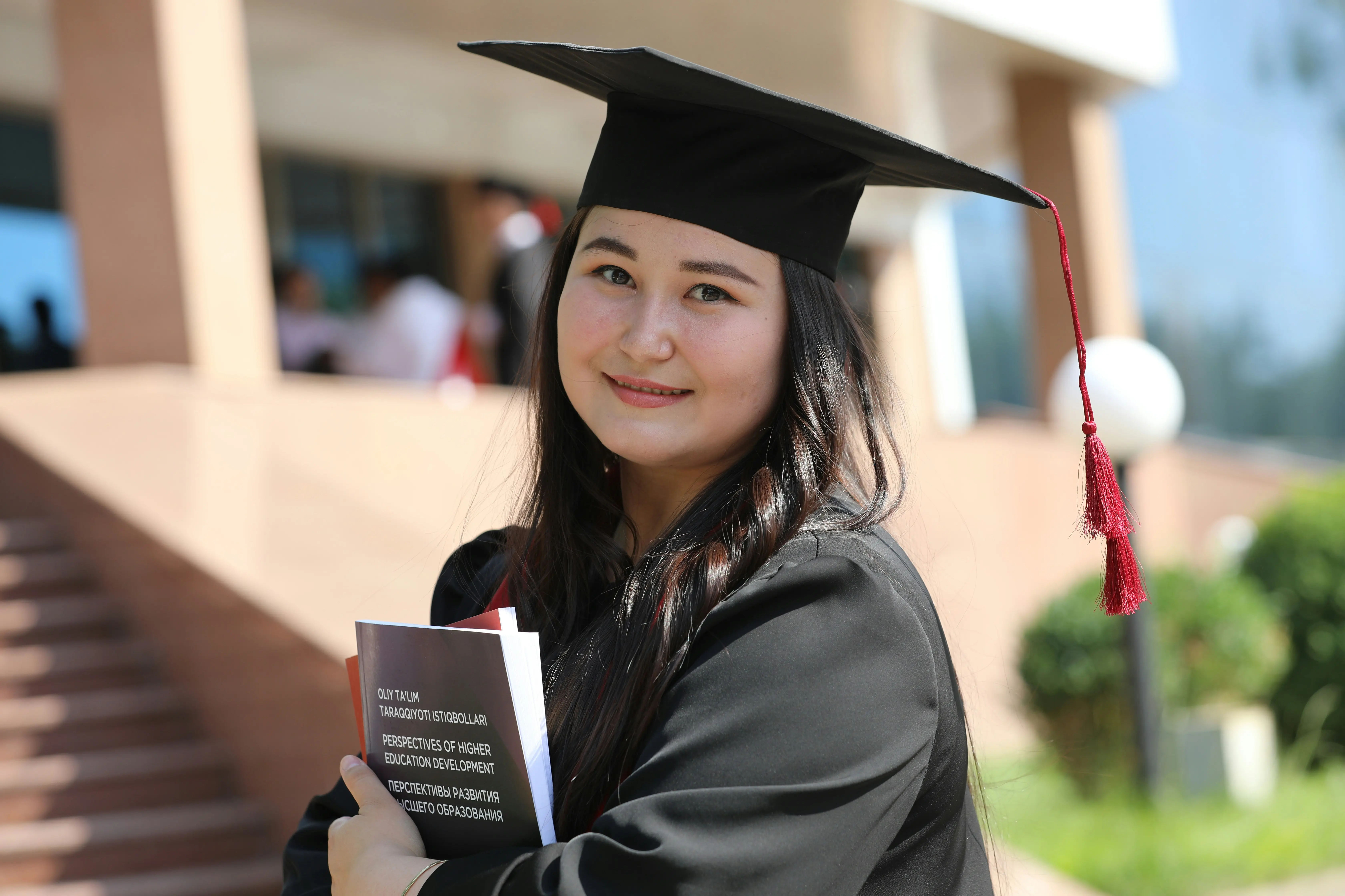 Étudiante diplômée tenant des livres universitaires devant un campus universitaire