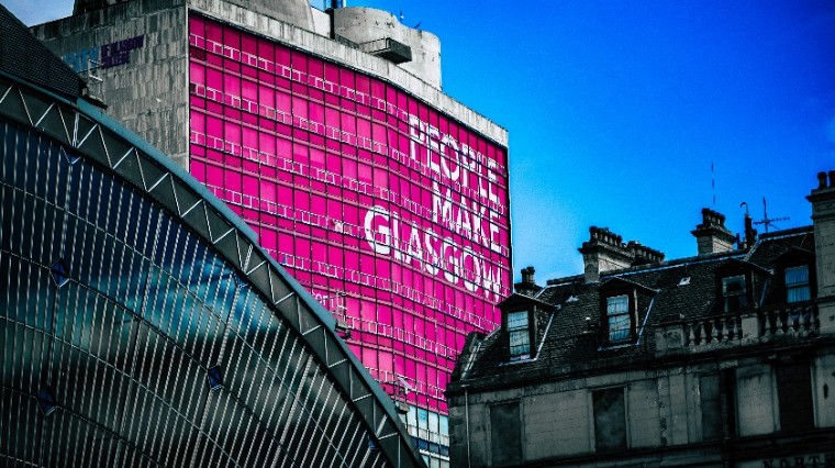 Building in London with a bright pink facade displaying the message “More Than Glass,” surrounded by city architecture.