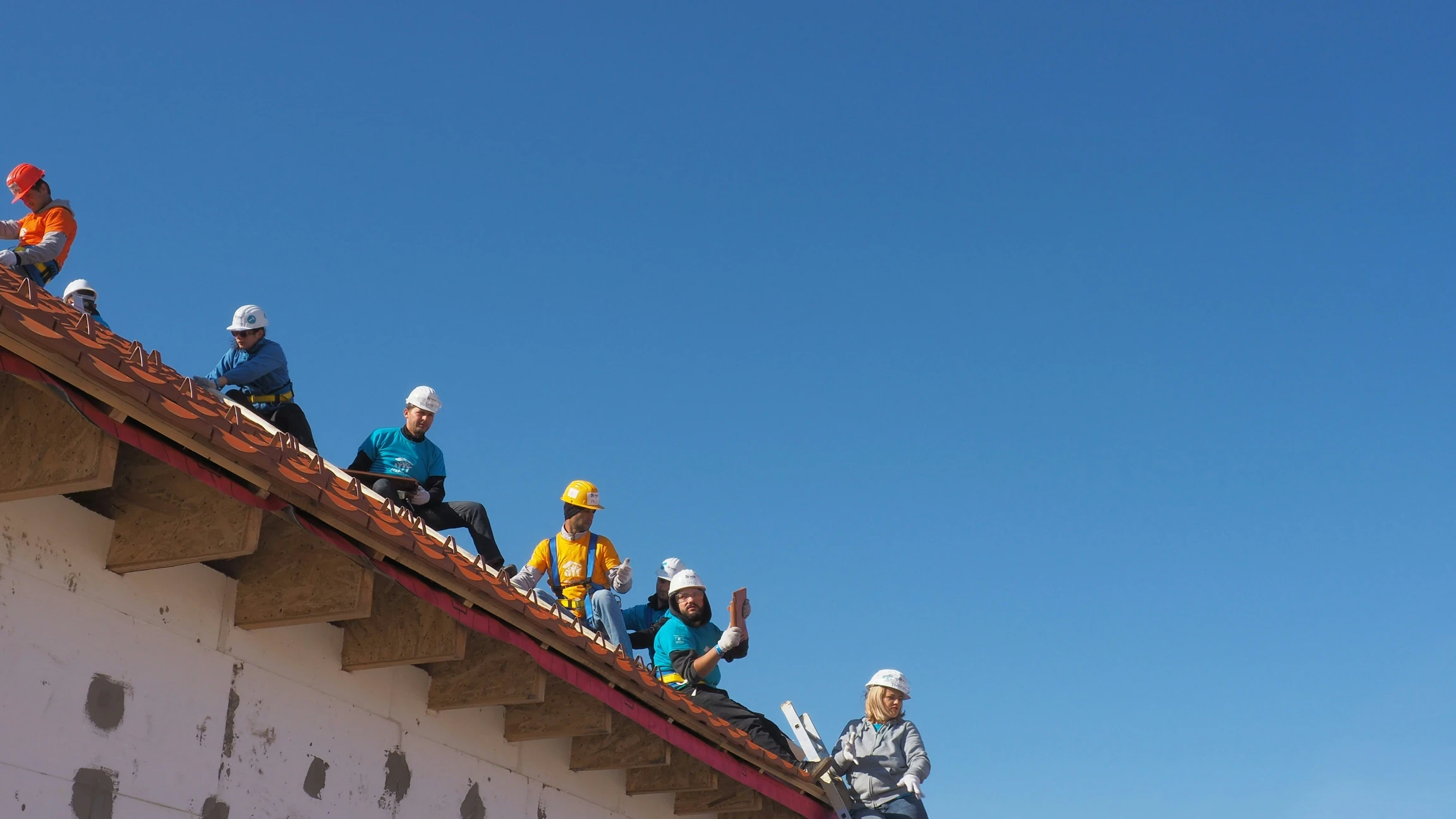 Workers in helmets and safety gear sit on a roof under construction.