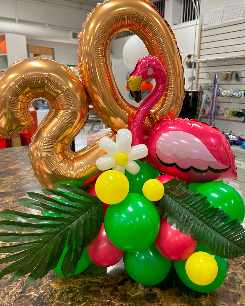 Tropical-themed balloon arrangement with gold number 20 balloons, green and white balloons, and palm leaf accents created by Be Bold Balloons