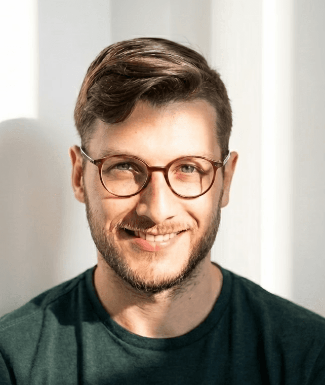 A woman with short curly hair wearing a black t-shirt looks into the camera.