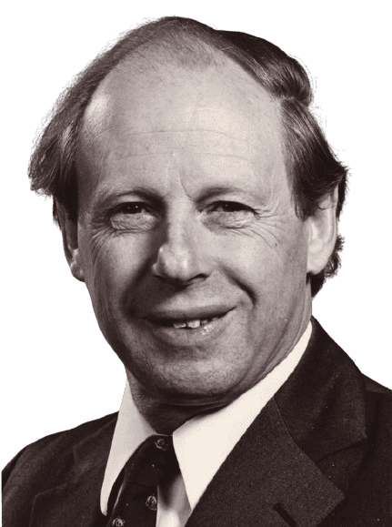 A black-and-white portrait of a middle-aged man with thinning hair and a warm smile, dressed in a suit and patterned tie. The close-up, formal pose highlights his friendly expression and conveys a sense of professionalism and experience, giving the image a classic, respectful tone.