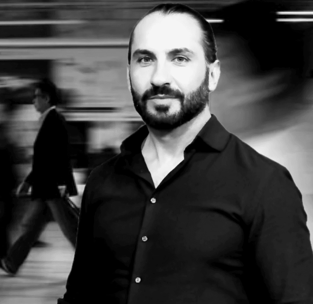 Black and white photo of a caucazian man with beard in a black shirt in a modern office interior