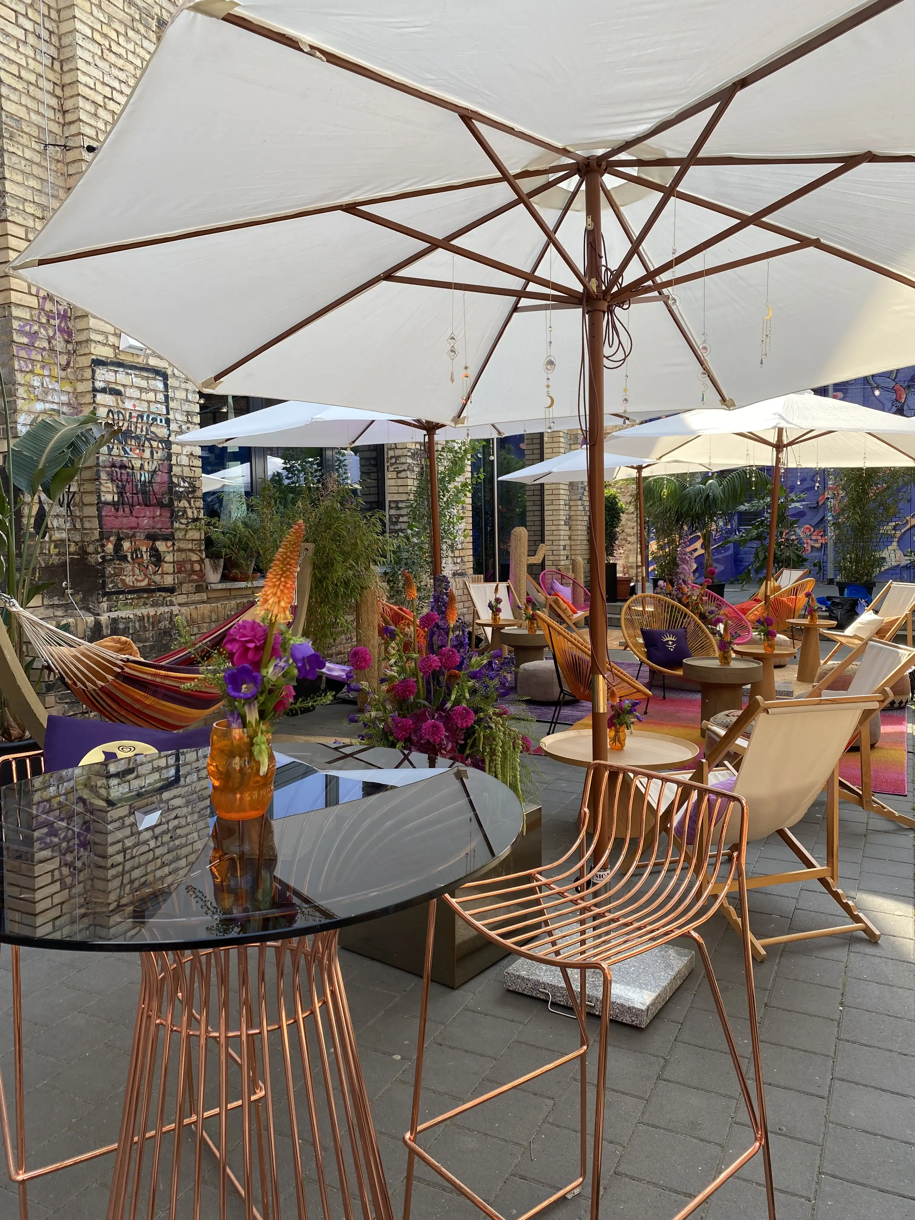 High table with glass top, copper wire chairs and flowers under cream parasols at the Magnum event.