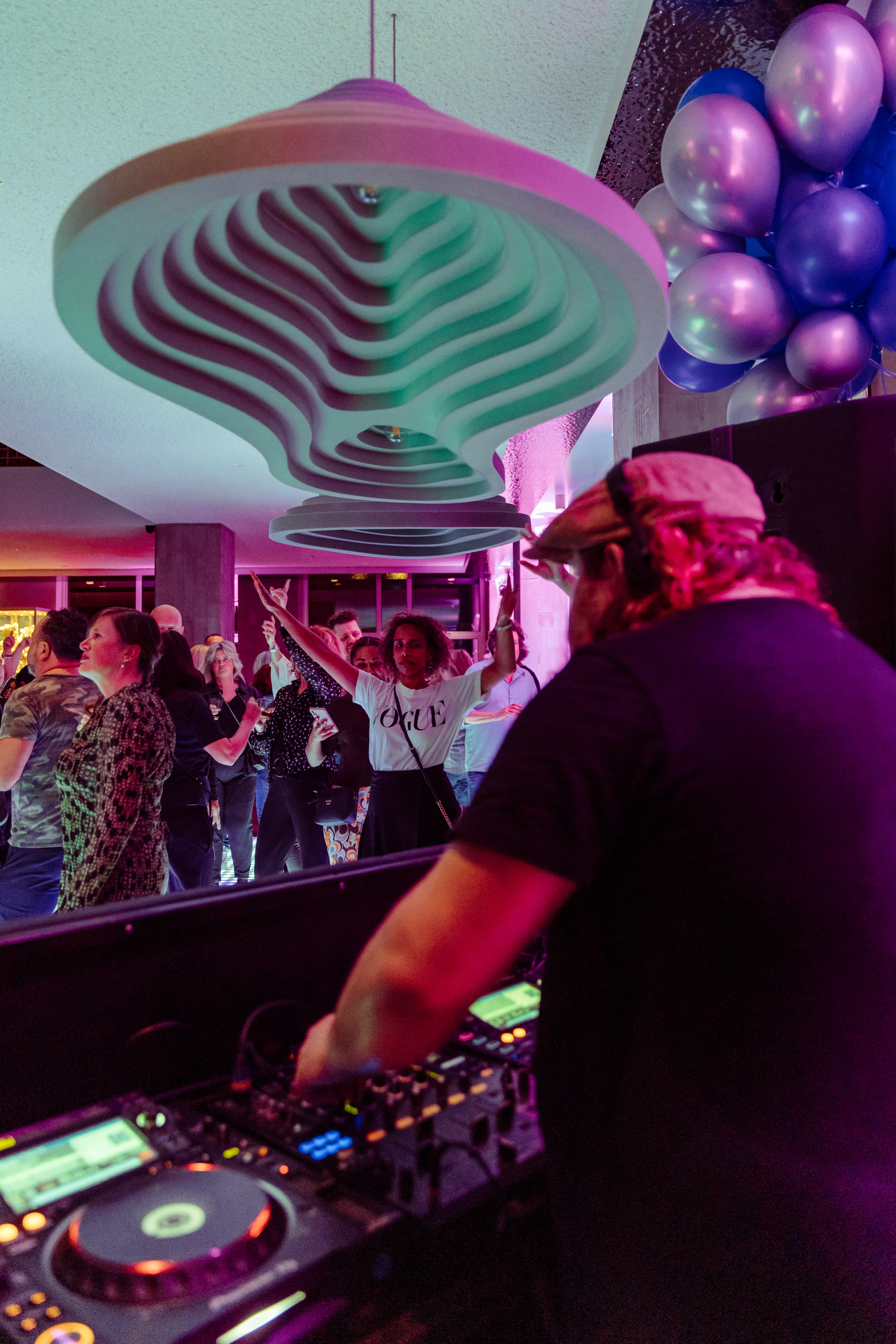 A DJ performs at a lively event, with colorful lights and an enthusiastic crowd in the background.