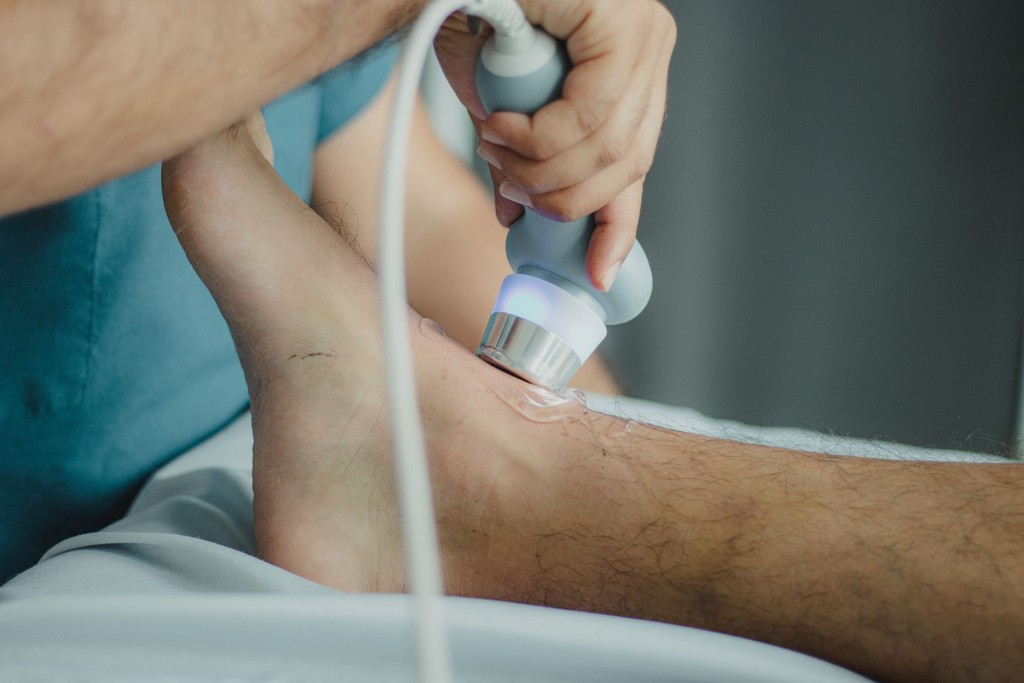 A shockwave therapy applicator being used on a patient's ankle.