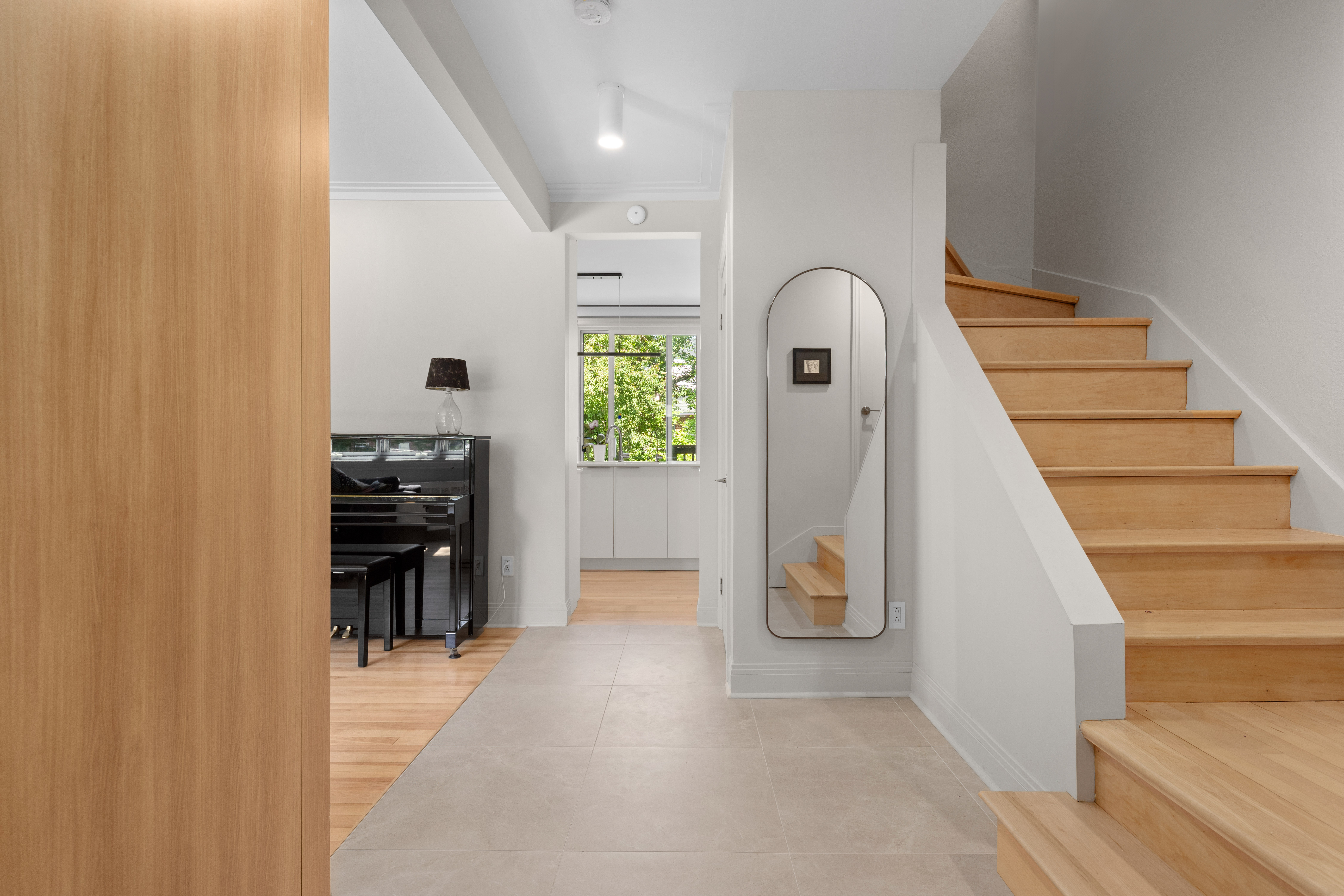 A softly lit hallway with a series of arched doorways, warm-toned walls, and wood flooring leading toward a seating area with neutral furniture.