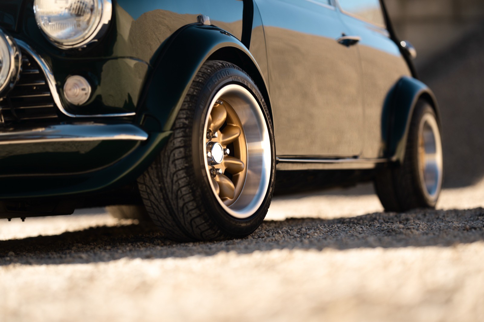 A small, green and black vehicle parked on a sandy surface, with a warm sunset lighting the scene.