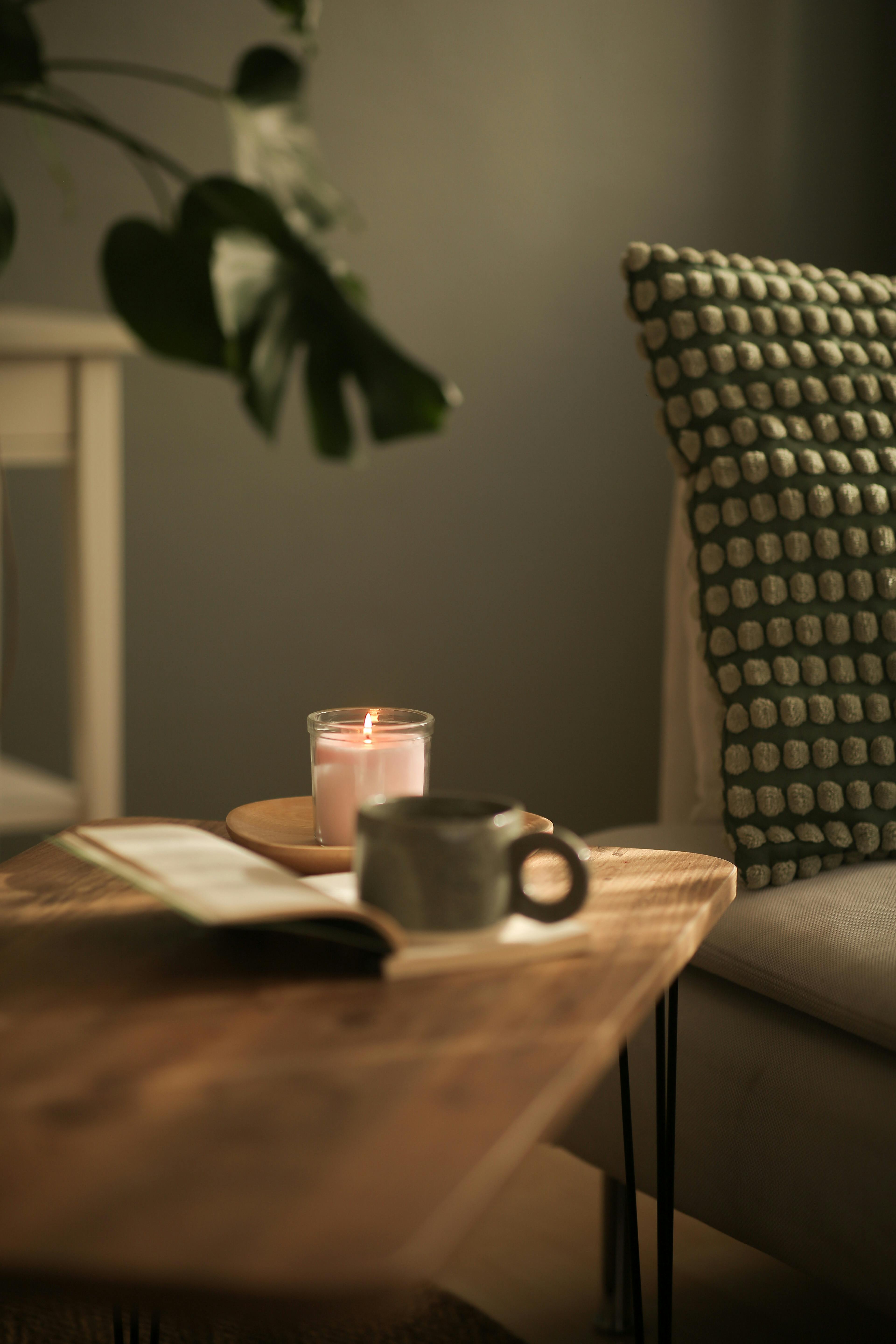 A photo in shades of green and brown, featuring a table with a mug, a book, and a candle on it.