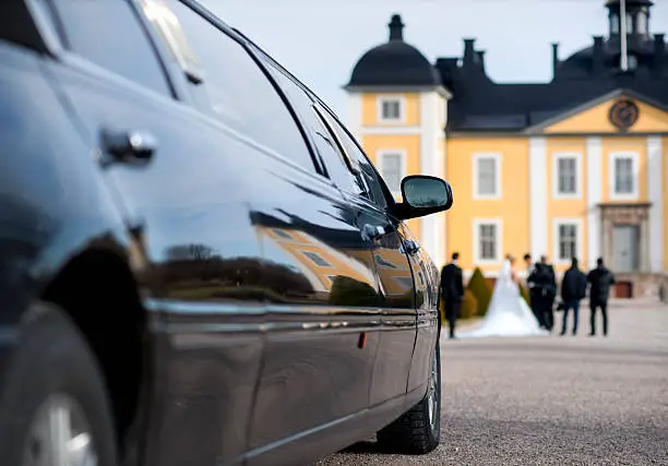 Professional black limo waiting to transport the bride and groom outside of a mansion. 
