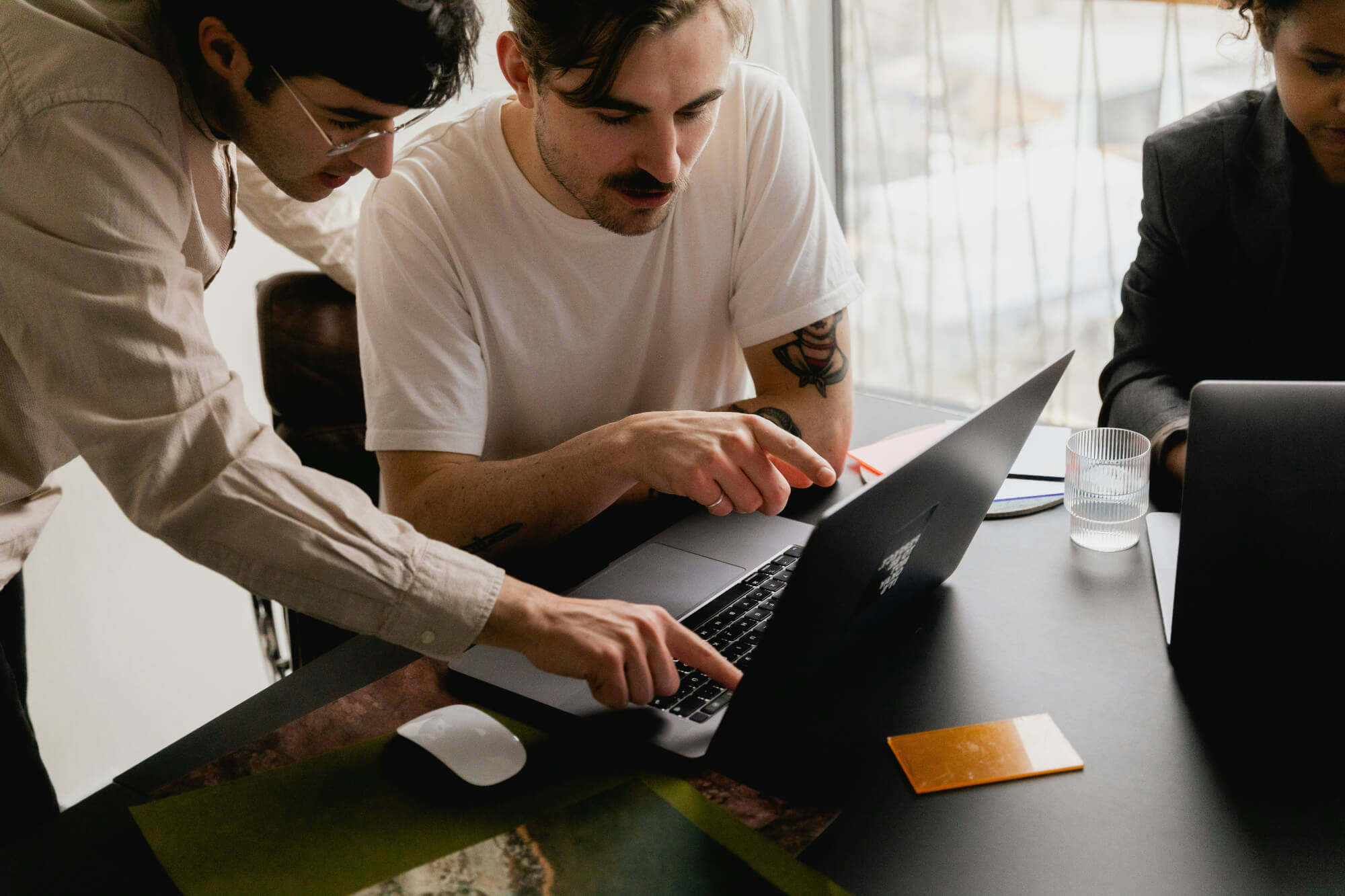 Two people focus on a laptop screen in a collaborative office setting. 