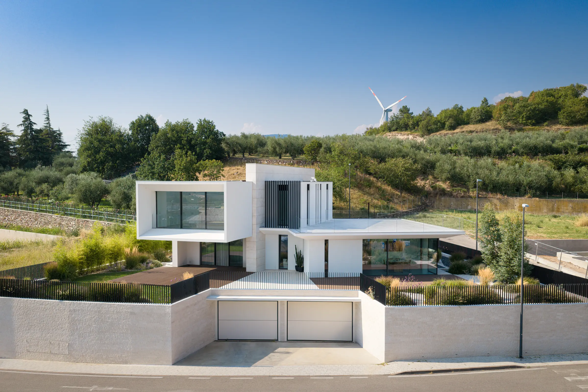 Edificio bianco dalle forme squadrate con ampie vetrate, immerso tra gli ulivi di una collina