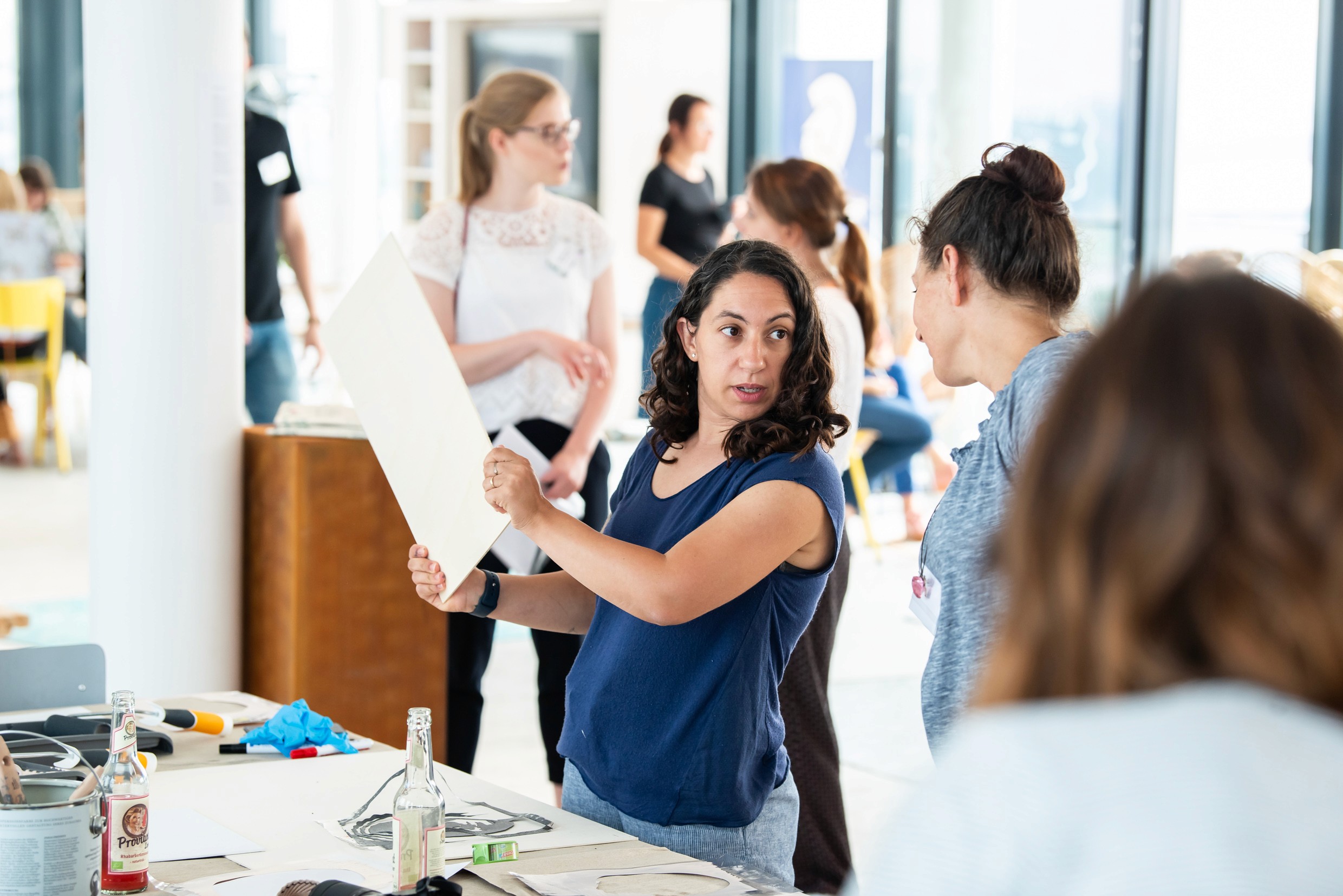 Großer Kreativ-Workshop mit Teilnehmerinnen an langen Tischen in einem lichtdurchfluteten Glashaus.