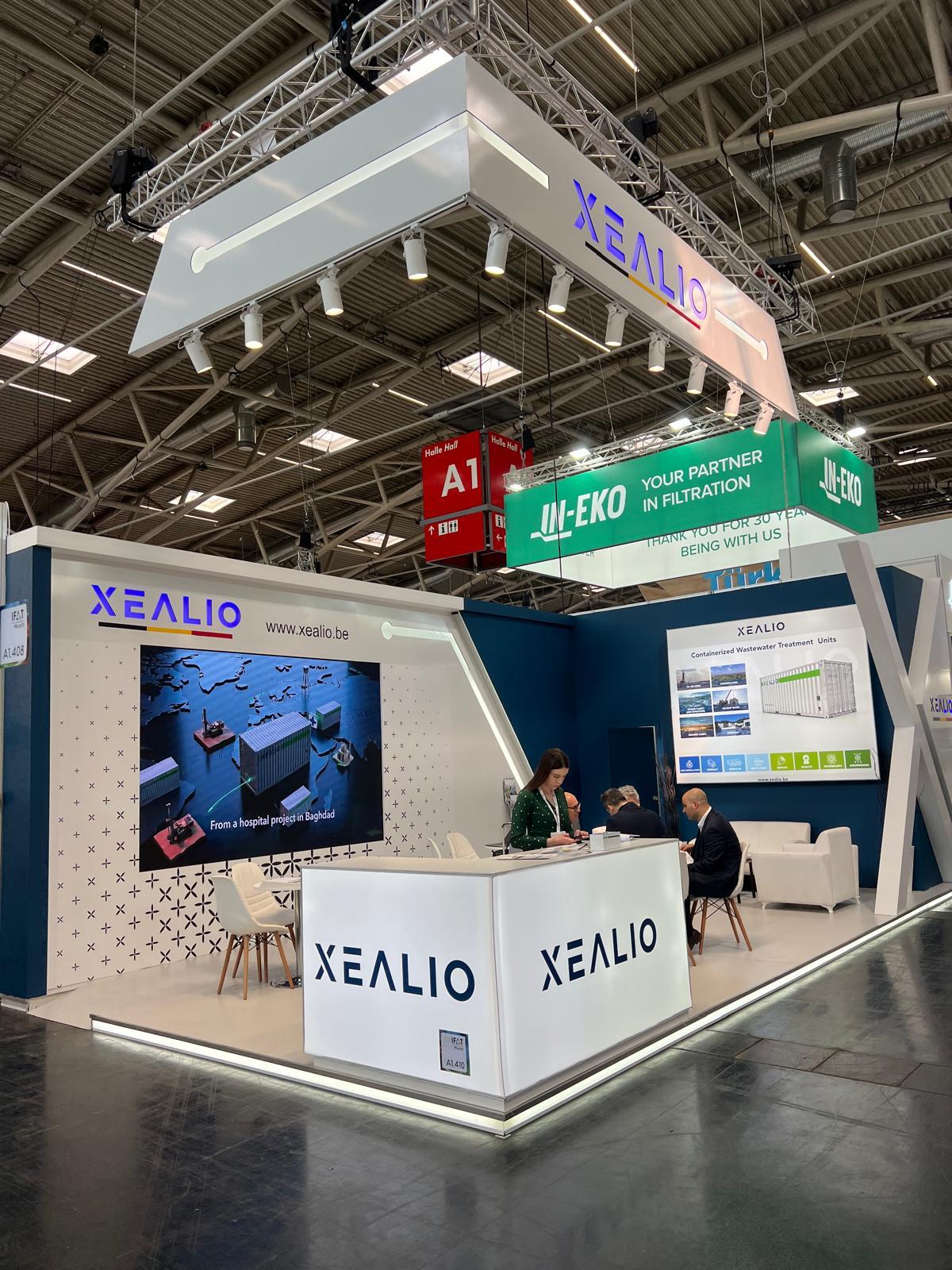 Hanging banner above the Xealio stand, continuing the X-shaped design language for consistent brand recognition across the booth structure and overhead branding.