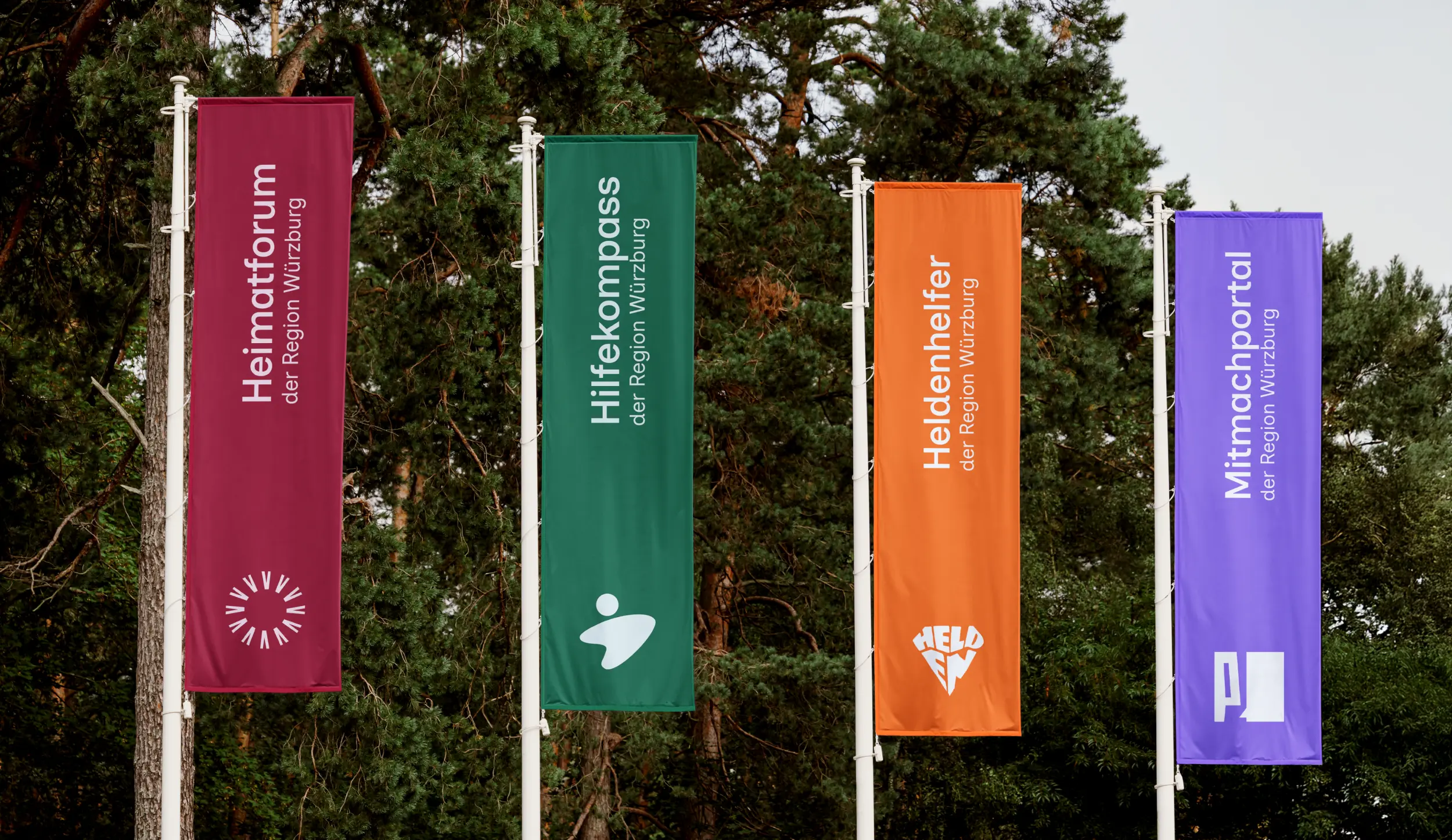 Vier Werbefahnen zu Heimatforum, Hilfekompass, Heldenhelfer und Mitmachportal vor grünem Waldbild.