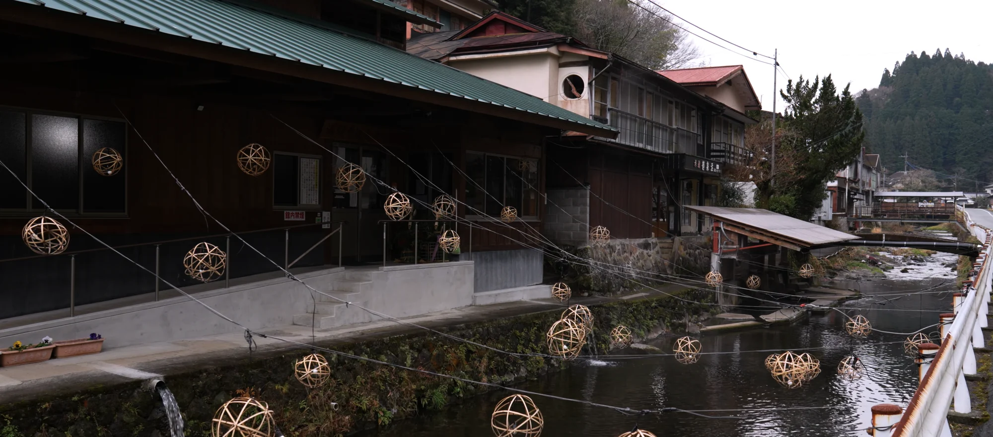 Unlit bamboo lantern spheres installed along a river channel in daylight