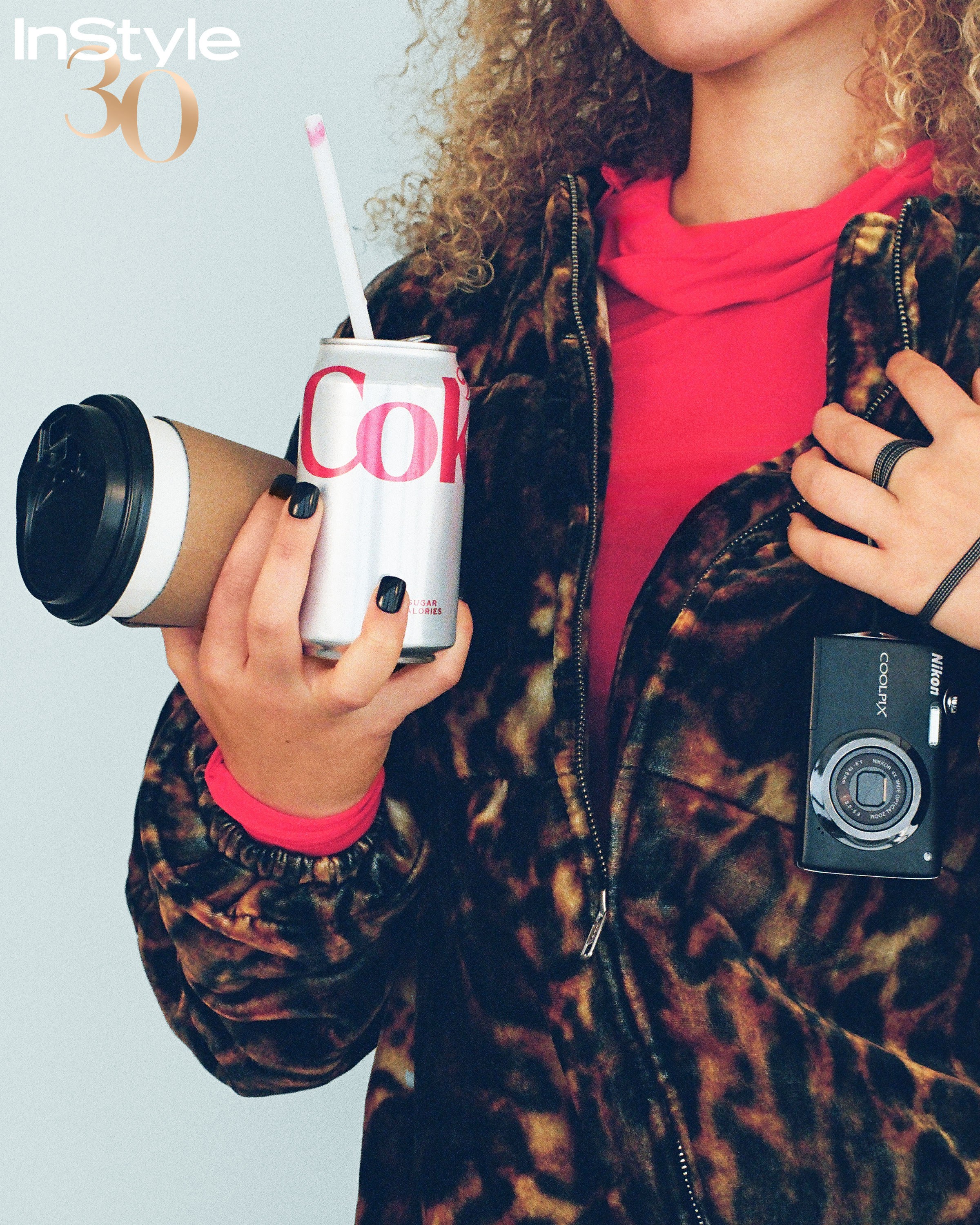 Dark indie sleaze manicure holding coffee and Diet Coke beside a compact camera and leopard print jacket