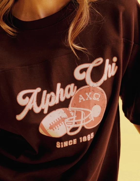 Close-up of a burgundy Alpha Chi T-shirt with a distressed football and helmet graphic.