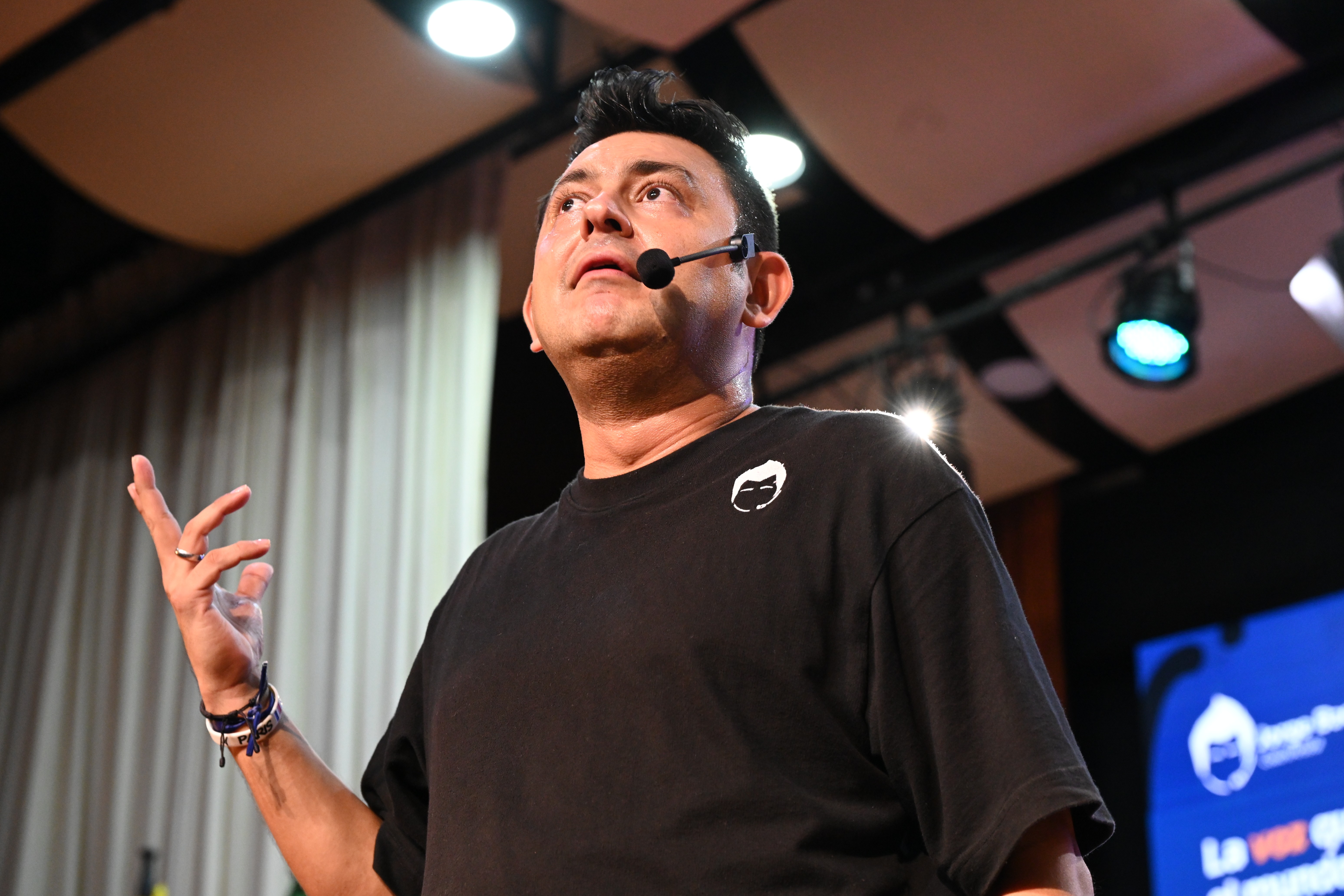 Jorge Baena en el escenario, con micrófono de diadema, levantando una mano