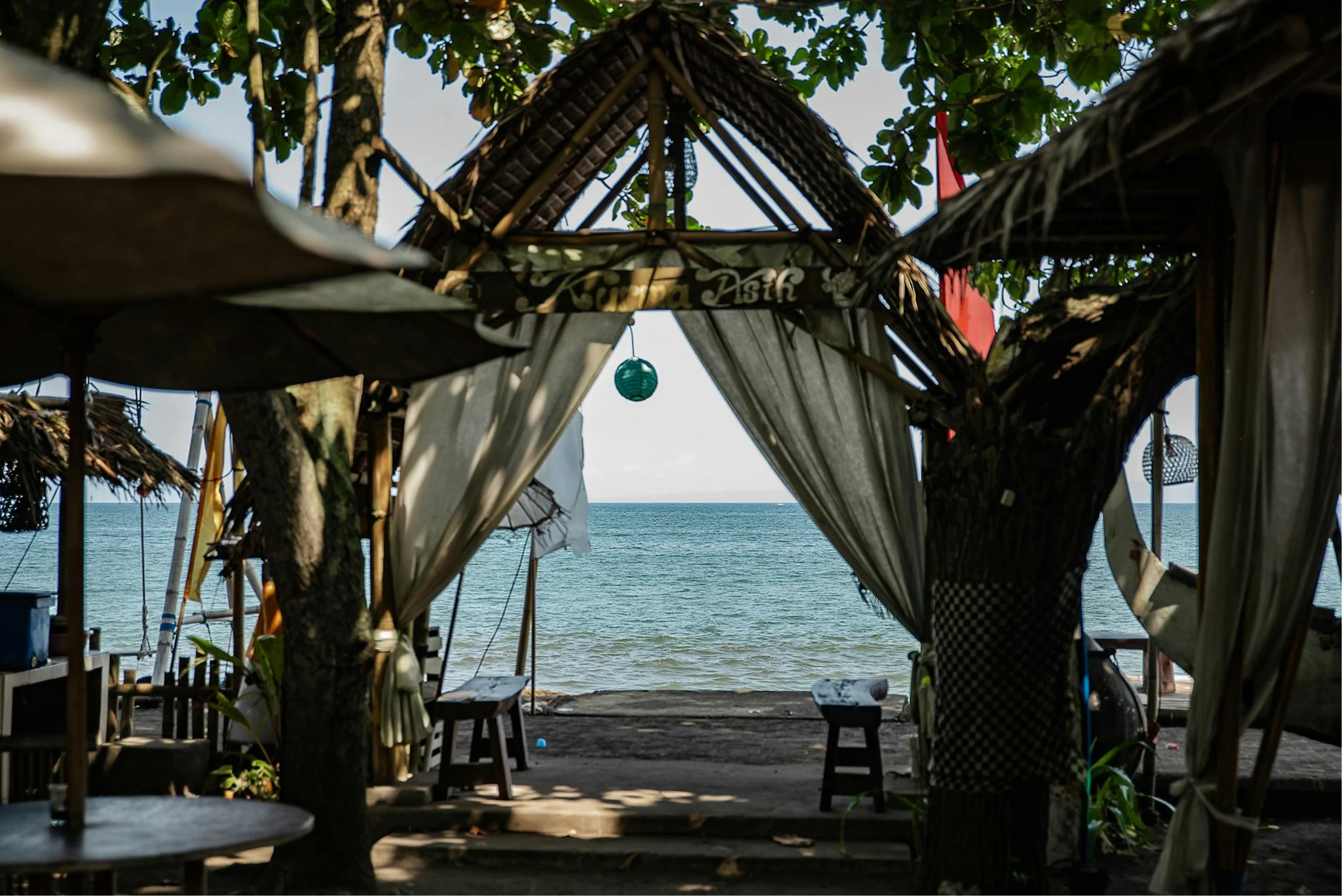 Beachfront cabana with white curtains opening toward the ocean.