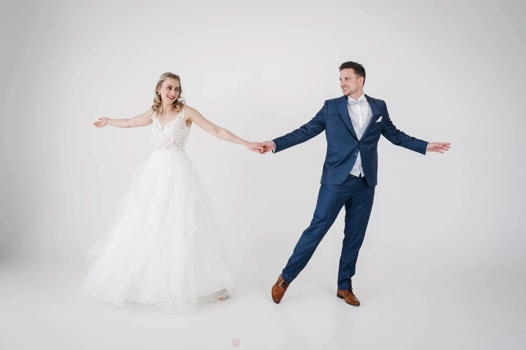 Brautpaar hält Hände im Fotostudio Erfurt, sie in Spitzenkleid, er in blauem Anzug, vor hellem Hintergrund.