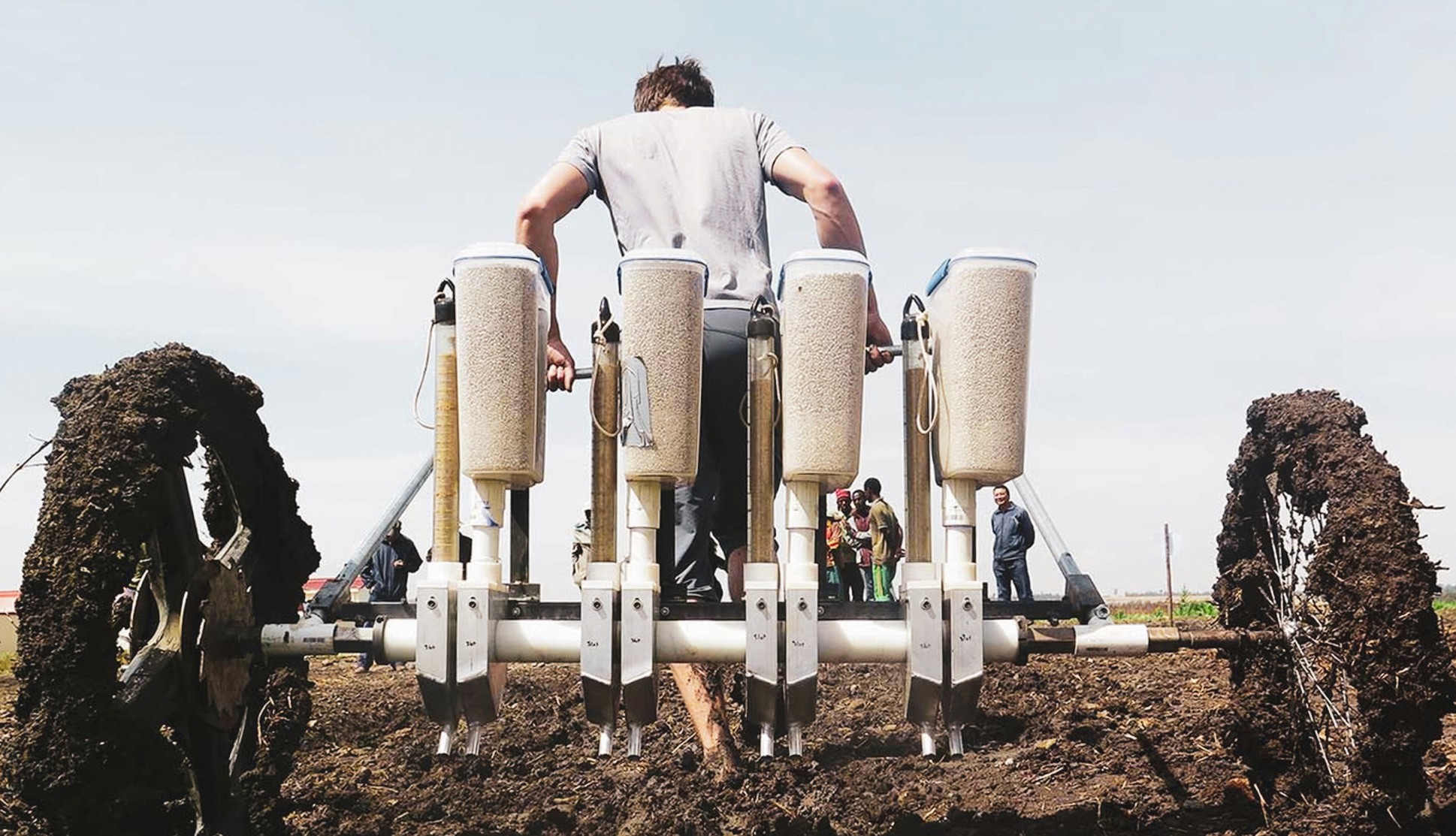 Man pulling teff planter in muddy field.