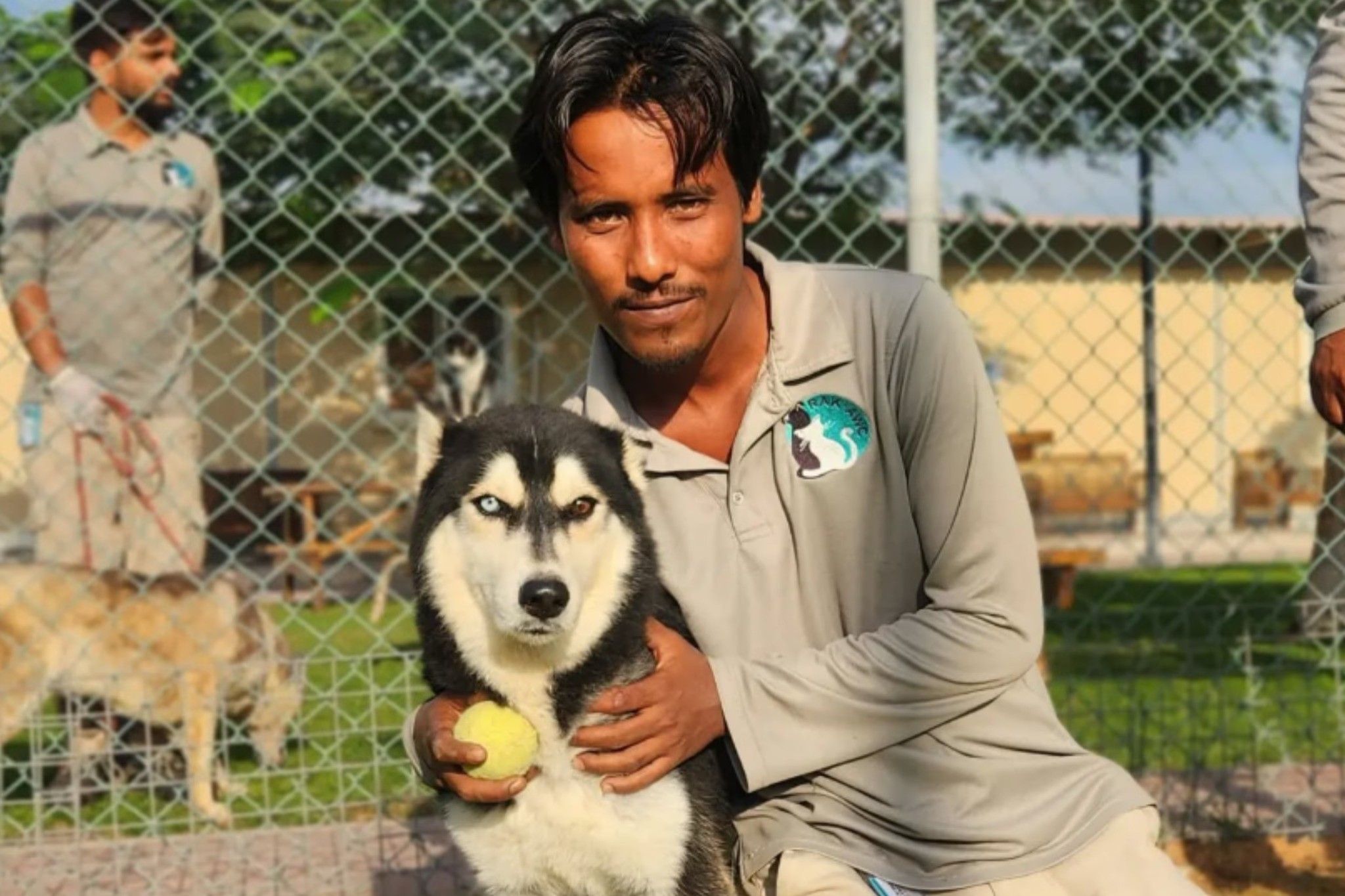 A dog handler is posing next to a dog while holding a tennis ball.