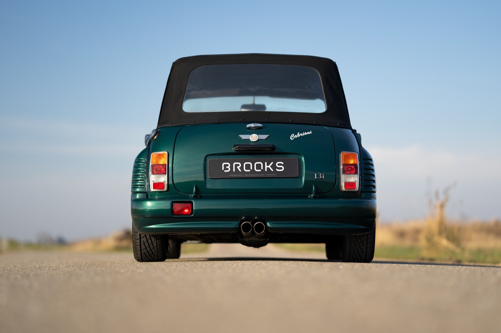 A green classic car parked on a deserted road with a clear blue sky in the background.