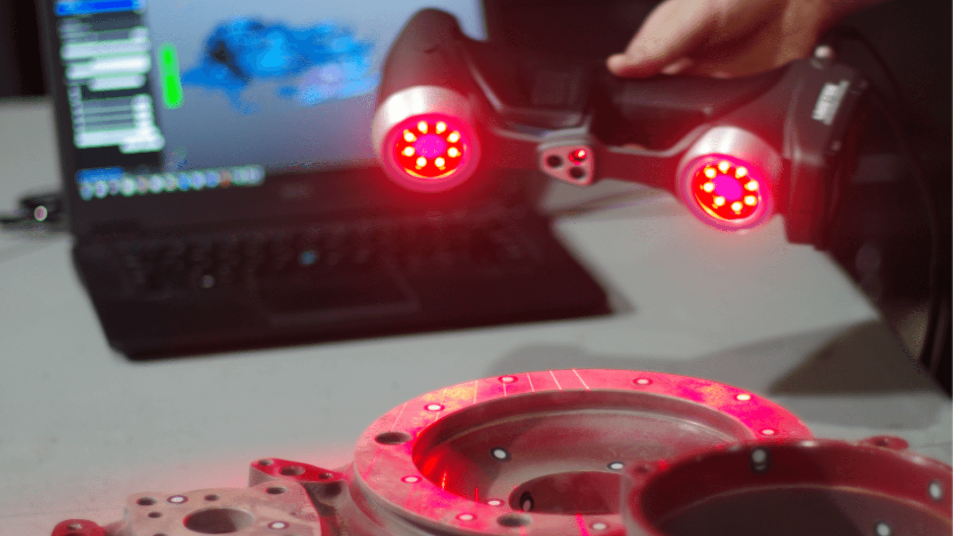A man stands while two people sit at a table in an office setting, smiling and engaged in conversation. The mood is friendly and collaborative.