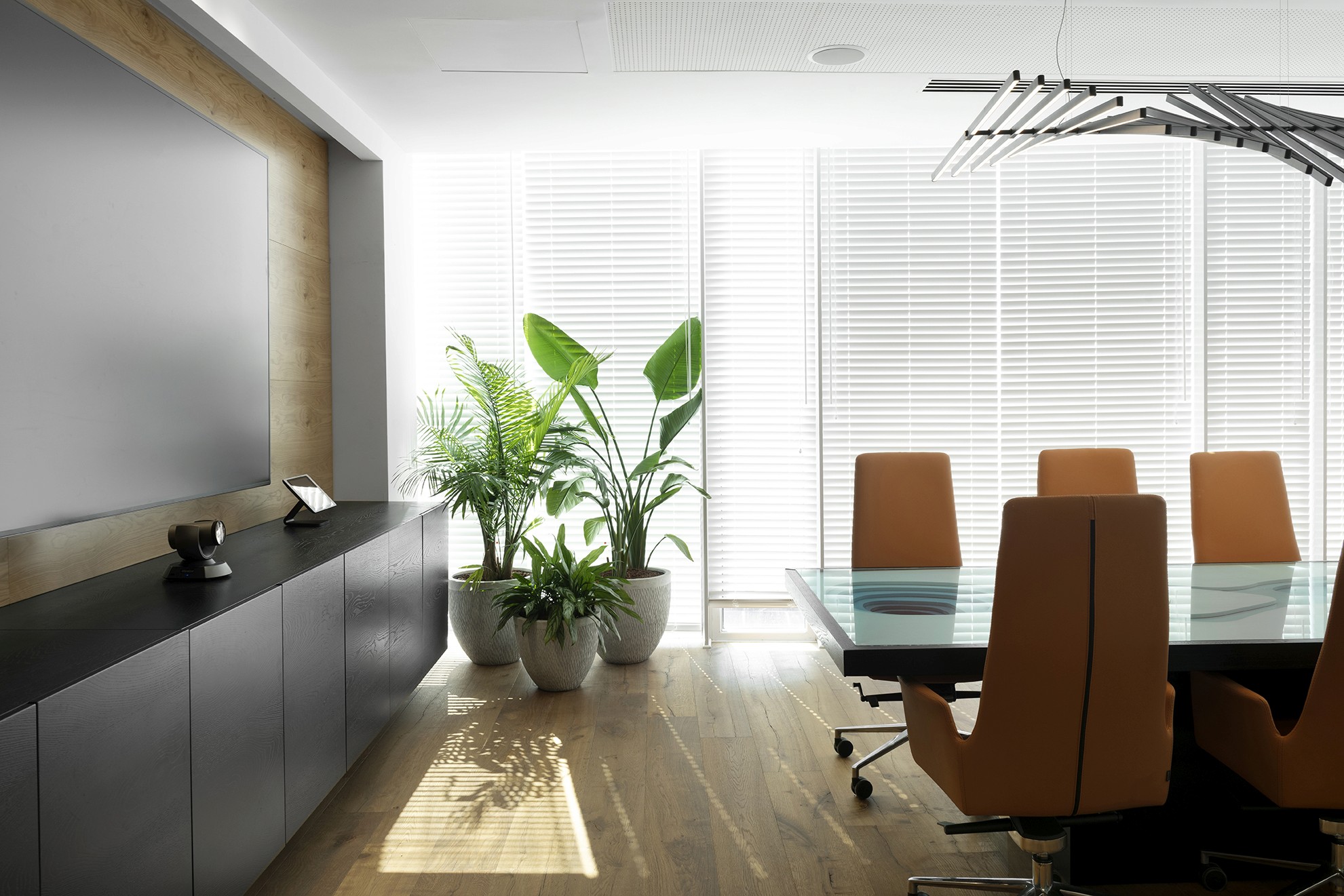 עיצוב חדר ישיבות: שילוב של גוף תאורה לינארי מרחף מעל שולחן הטופוגרפיה, מוקף בכיסאות עור יוקרתיים וחלונות עם תריסים ונציאניים.