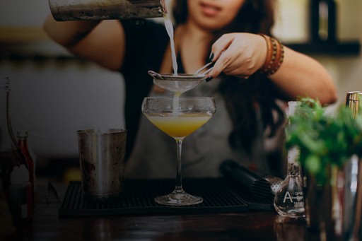 Foto de una bartender preparando una bebida en una copa martini de cristal  usando un colador y un shaker