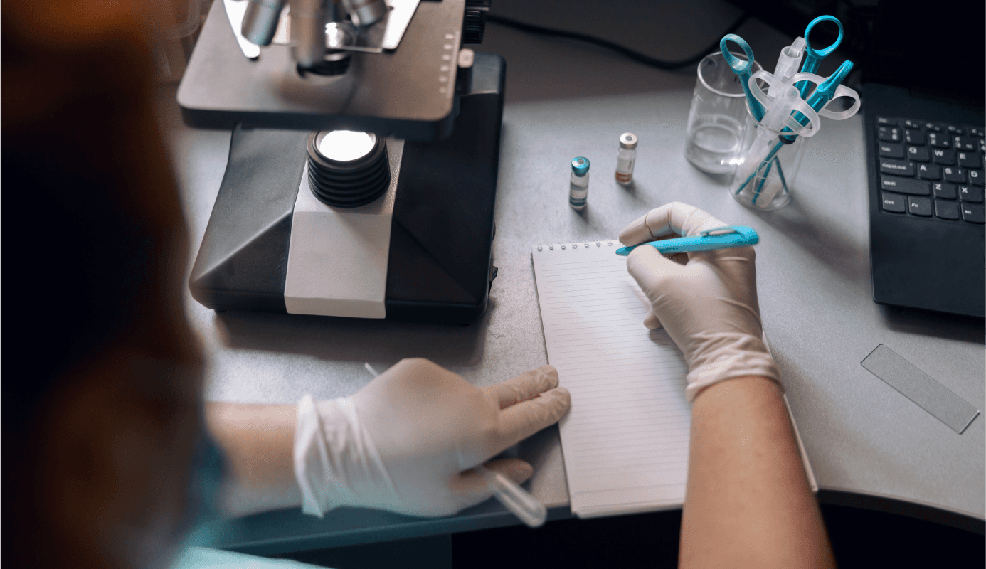 Researcher writes notes next to a microscope in a lab.