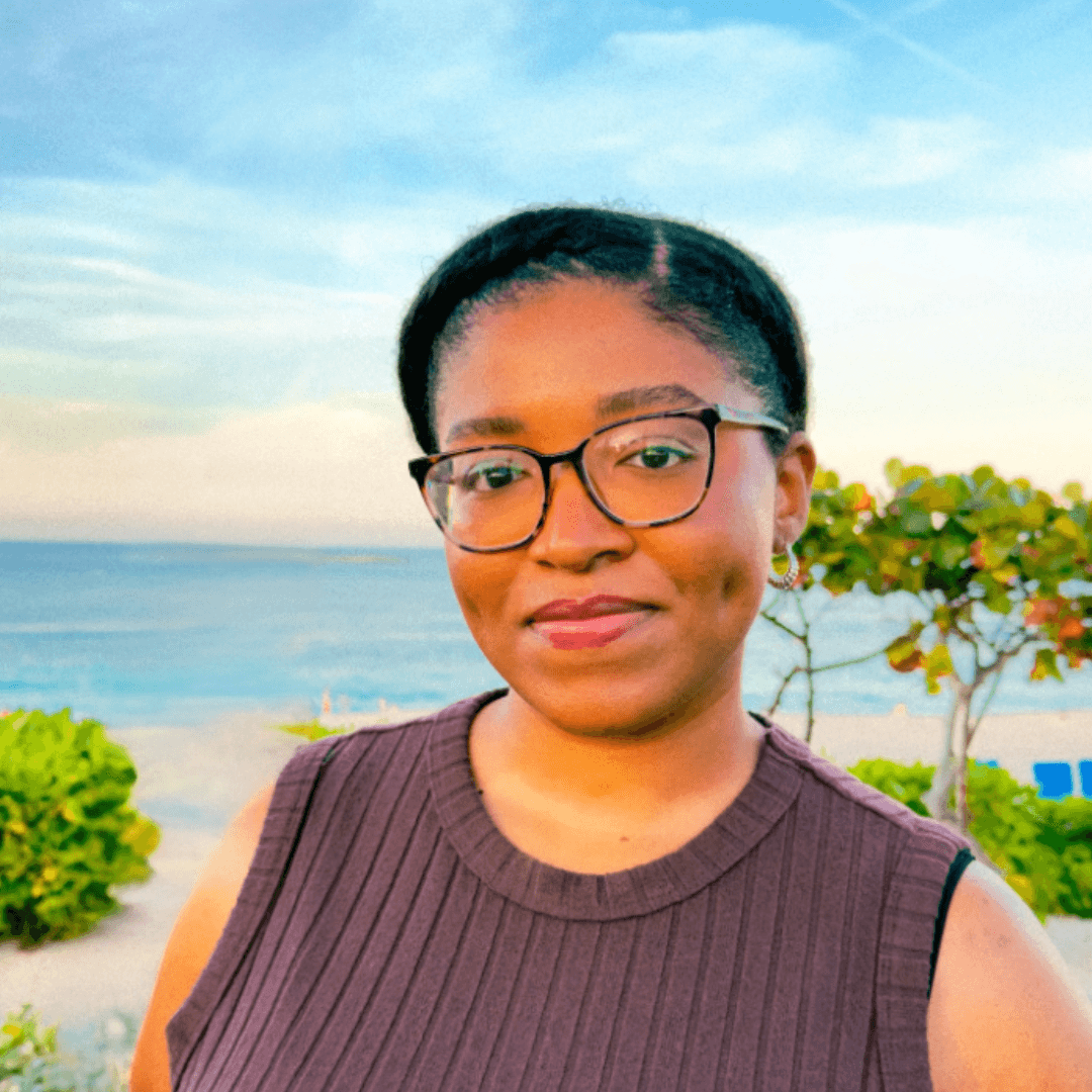 A picture of Kiana Price smiling with glasses on in front of a tropical beach at sunset.