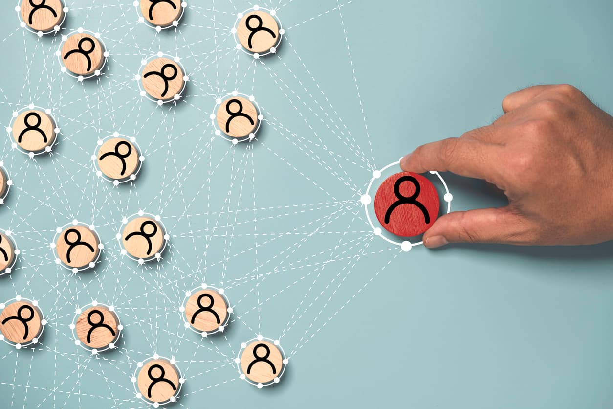 Hand selecting a single red figurine node connected to a network of light wooden figurines, illustrating cross-functional leadership and stakeholder networks