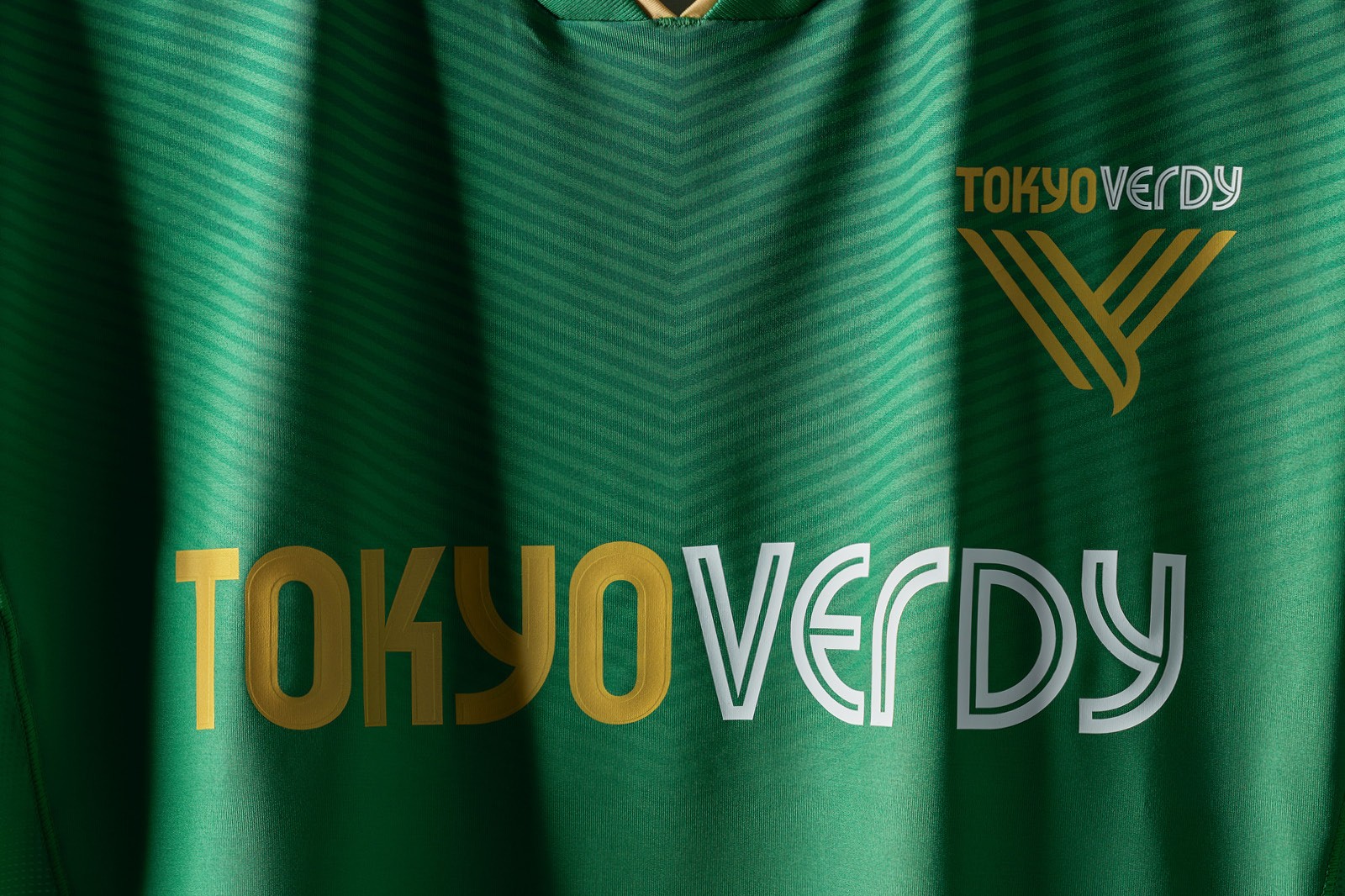 A green Tokyo Verdy soccer jersey with yellow and white stripes, featuring the team's logos prominently displayed across the chest.
