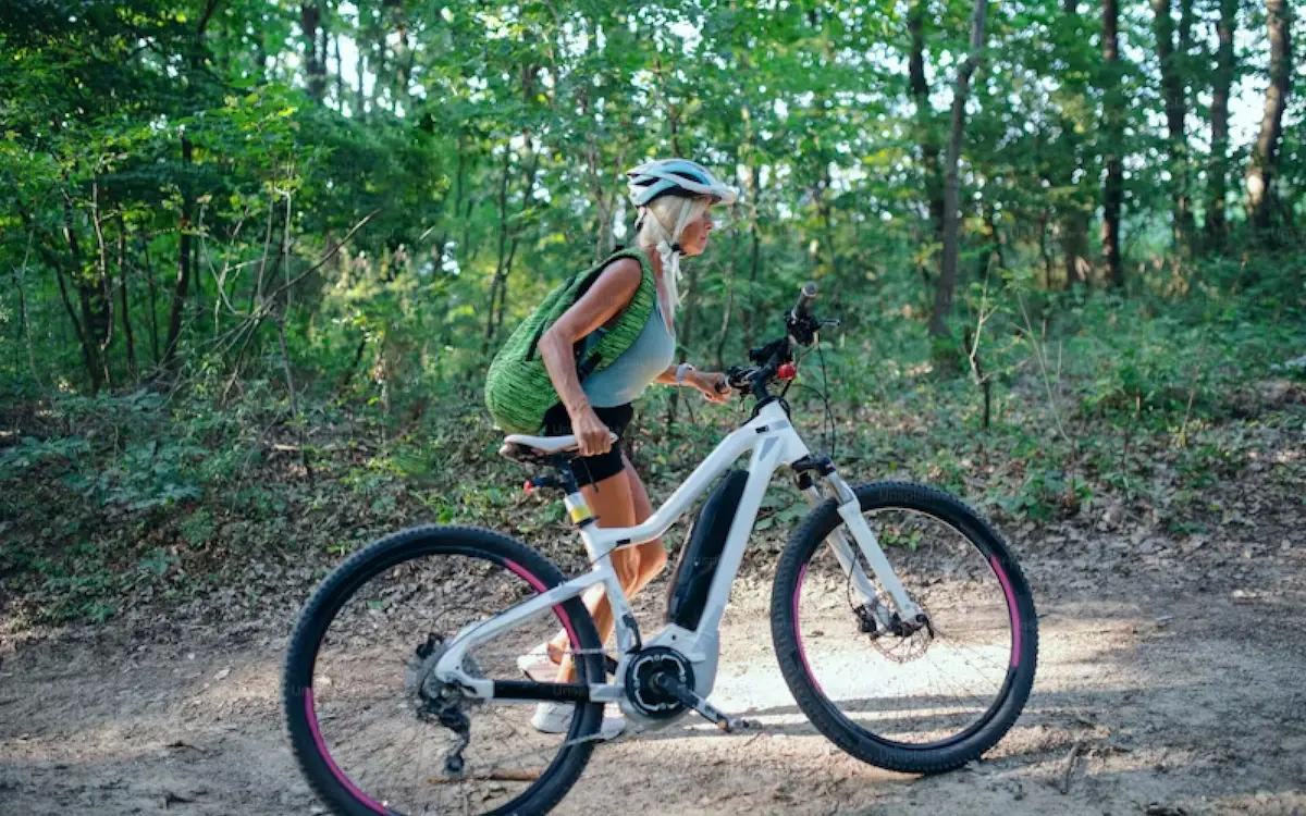 A photo of a cyclist pushing a battery powered bicycle through a wooded area