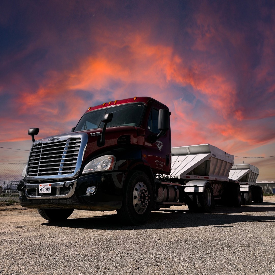 Hero image of a Red Double Bottom dump parked beneath an epic sunset and fiery golden sunset sky in the High Desert