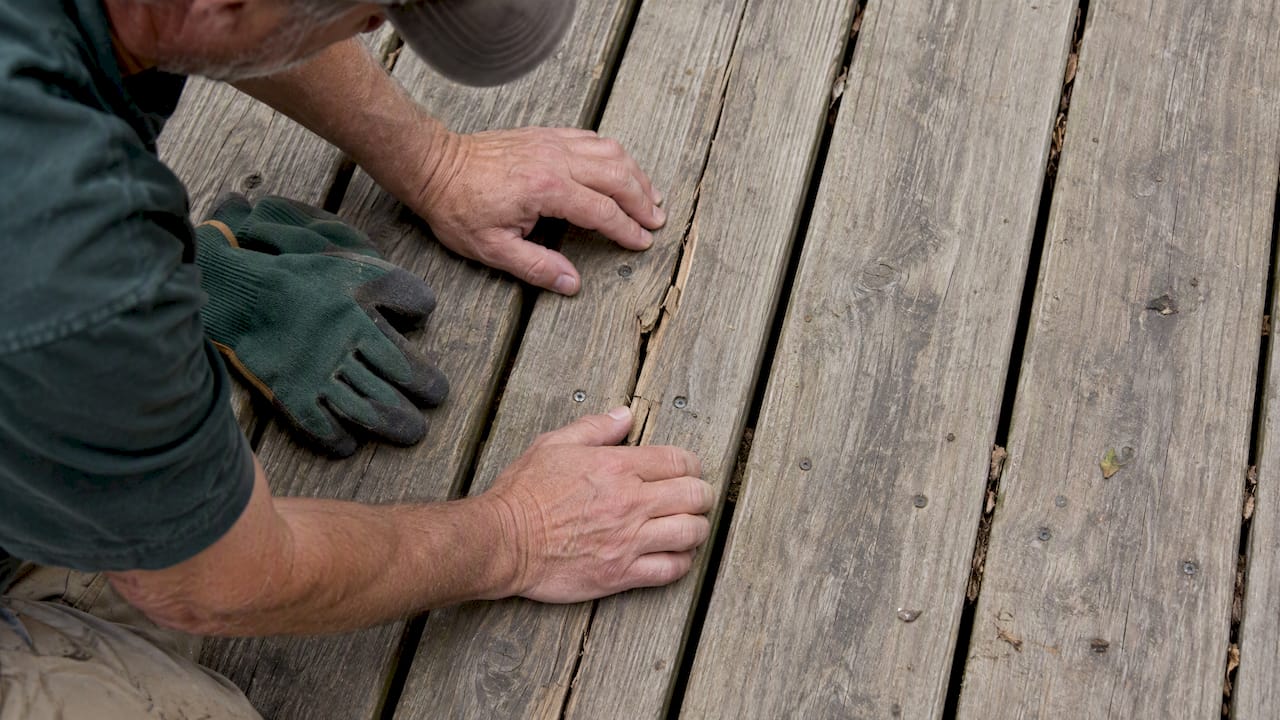 Homeowner inspecting cracked wooden deck board