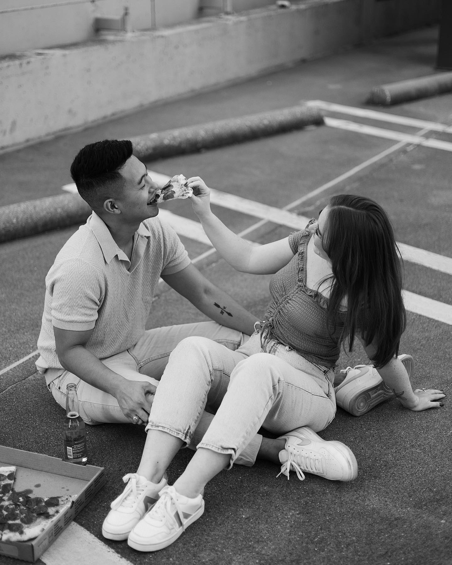 Black and white photo of a couple sitting on the ground eating pizza.