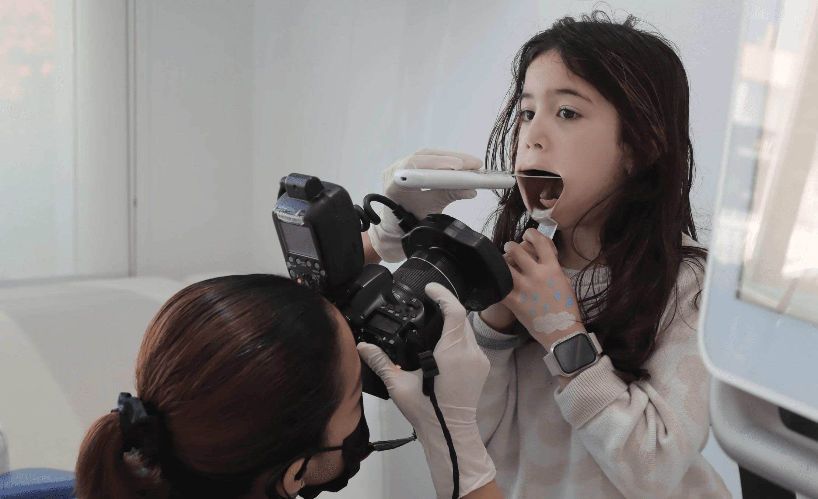 A dental professional takes an intraoral scan of a young girl's mouth, checking for cavities in baby teeth.