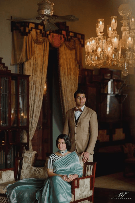 Elegant couple posed in a vintage-inspired room with ornate chandeliers and furnishings, evoking the glamour and refinement of vintage wedding photography.