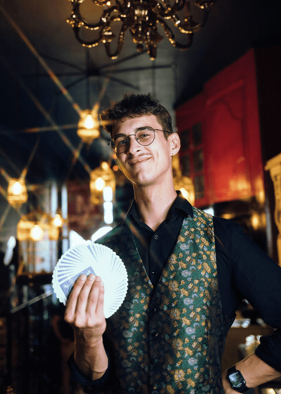 Zdjęcie magika Filipa, który. z uśmiecham trzyma karty w wachlarzu.