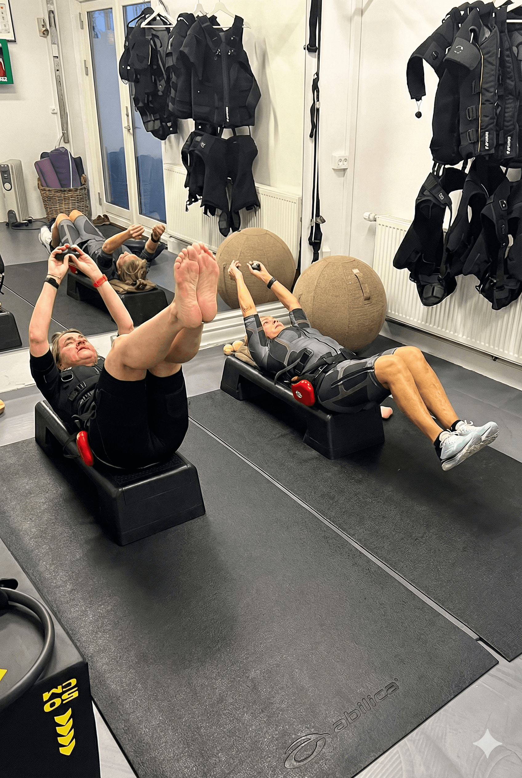 A shirtless man intensely using battle ropes in a gym, with another man in the background.