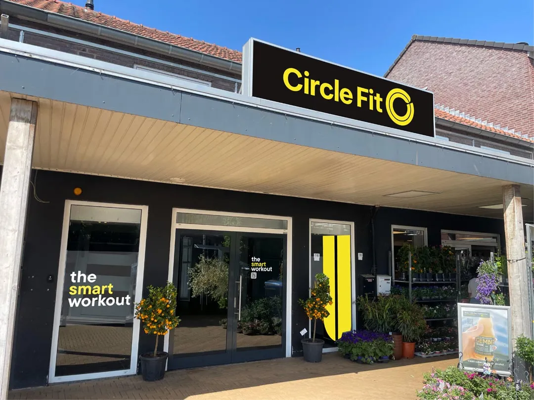 A Circle Fit hub with large windows, a sign above, and a path lined with plants and flowers in front.
