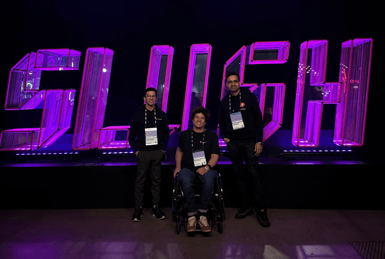 Sociability team members in front of a pink fluorescent sign reading ‘SLUSH’.