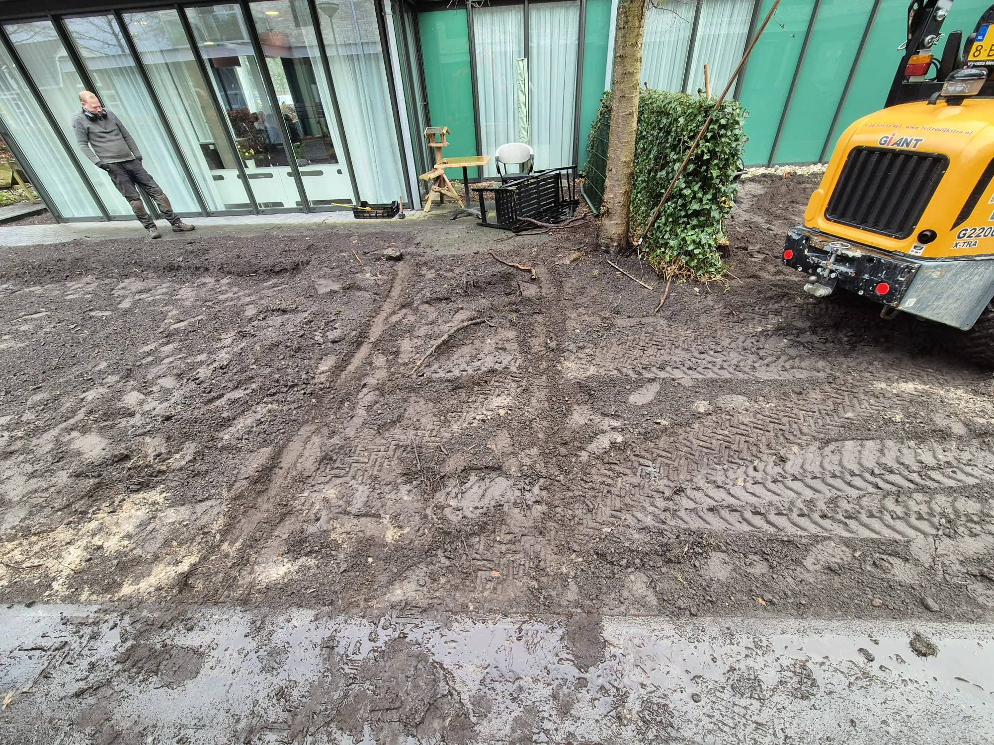 Bestaand grasveld met sporen van graafmachine en man bij zorglocatie, voorbereidend voor aanleg belevingstuin in Gorredijk.