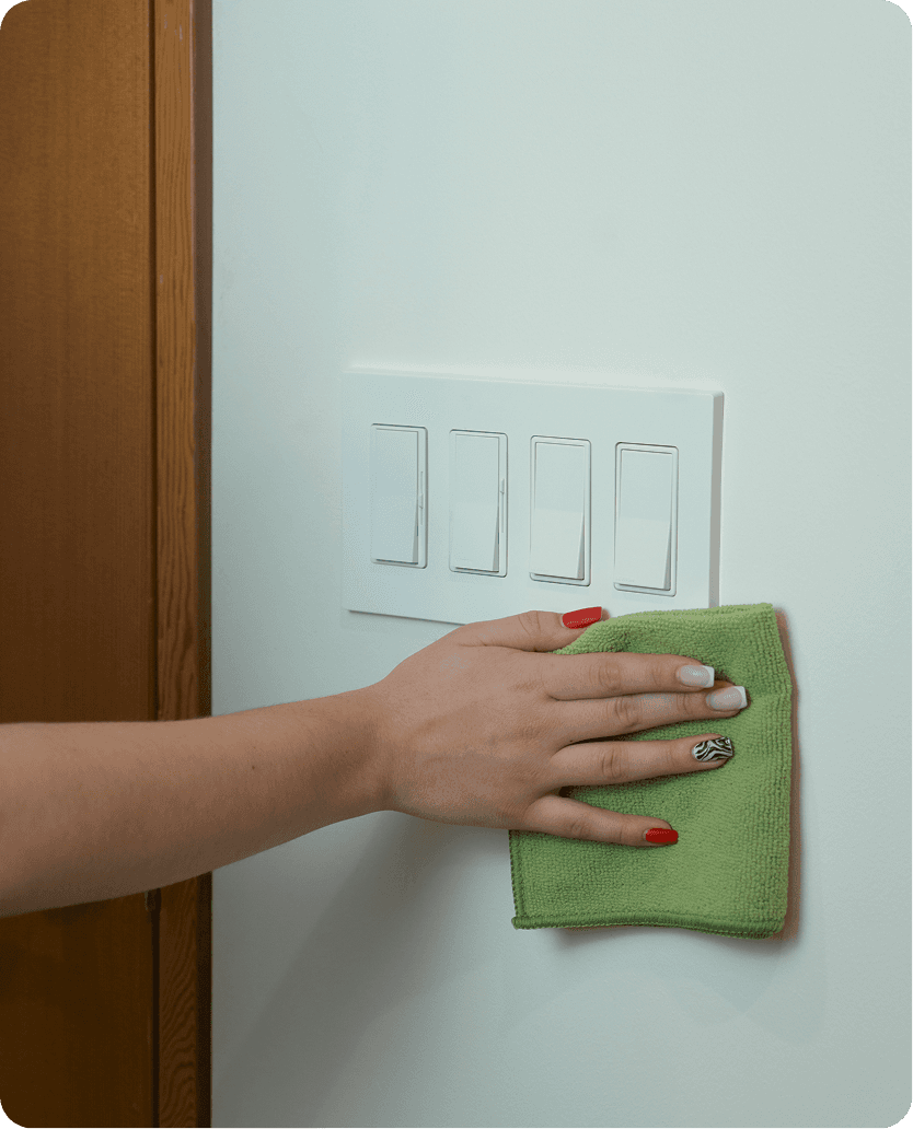 A cleaner is wiping the dust off the light switch with a cloth