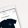 A tablet displaying a dark t-shirt on an online store. The t-shirt has a small logo on it.